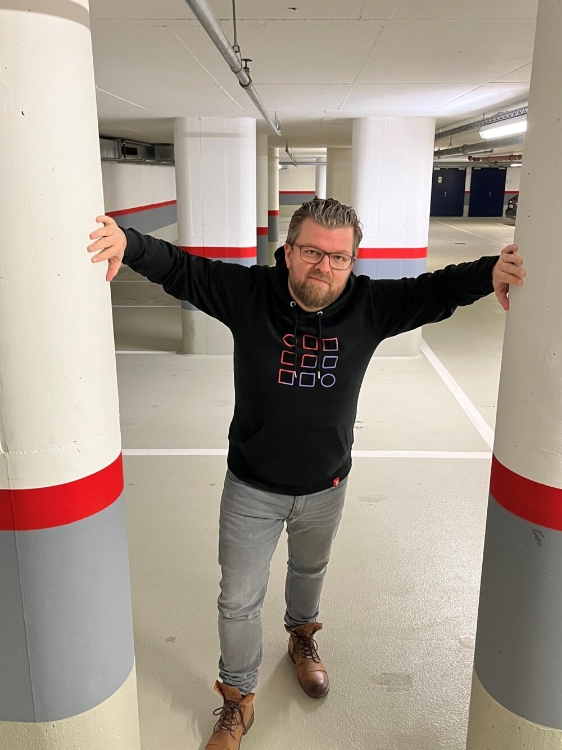 Männliches Model trägt schwarzen Hoody mit Kapuze und buntes Logo auf der Vorderseite